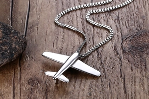 Detail of silver polished stainless steel airplane pendant on textured wooden background