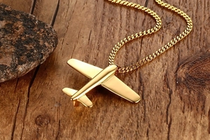 Close-up of polished gold airplane pendant on a link chain over a wooden surface