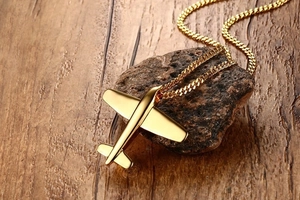 Detail of gold aircraft pendant and curb chain on a dark stone surface and wood backdrop