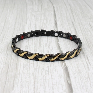 Magnetic therapy titanium steel bracelet with black and gold X-shaped links on wood background