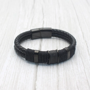 Men's woven black leather bracelet with magnetic metal clasp on a wooden background