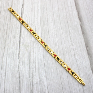 Détails d'un bracelet magnétique doré avec des inserts en pierres rouges noires et blanches