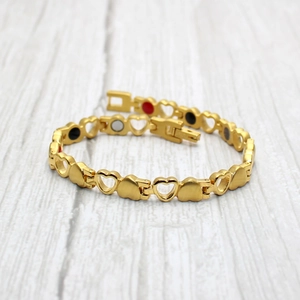 Gold magnetic heart bracelet for women with solid and hollow links on wood background