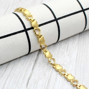 Elegant gold heart link bracelet with solid and hollow charms on a minimalist background