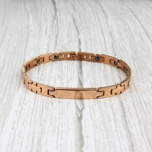 Bracelet magnétique or rose avec plaque rectangulaire sur bois gris texturé
