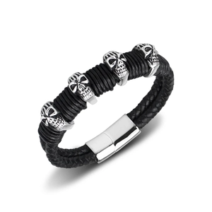 Macro detail of men's braided leather bracelet with silver skull charms and metal clasp