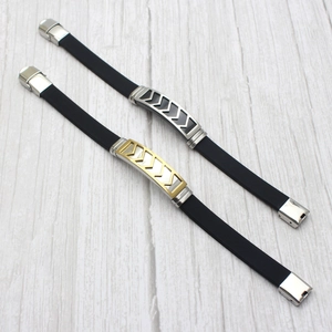 Close-up of men's black silicone bracelets with geometric arrow metal charms on wood
