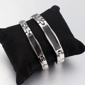 Pärchen-Armbänder aus Carbon-Titanstahl in Silber auf einem schwarzen Netzpolster