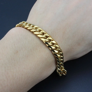 Polished gold Cuban link titanium steel bracelet for men shown on wrist over black background