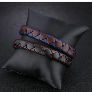 Detailed close-up of woven leather business bracelets on black satin display pillows