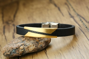 Close-up of men's black leather bracelet with gold geometric metal plate and silver buckle