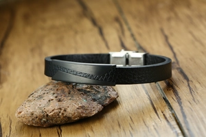 Detail of men's leather bracelet with black matte metal plate on natural stone background