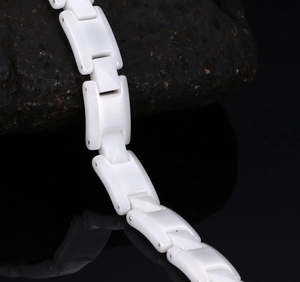 Macro detail of glossy white ceramic link bracelet on natural black stone texture