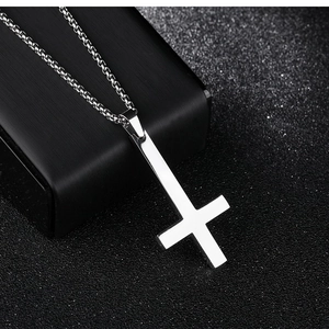 Close-up of a silver inverted cross pendant with a classic box chain on black background