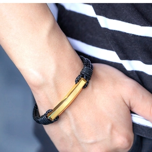 Gros plan d'un bracelet en cuir tressé noir pour homme avec curseur en métal doré poli