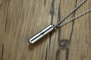 Detailed view of stainless steel cylinder pet urn pendant with laser paw print on wood
