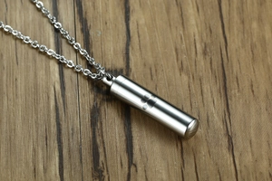 Macro view of a cylindrical stainless steel pet urn pendant with a laser dog paw engraving