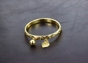 Detail of gold-plated bangle with sun engravings, heart pendant and small bell charm