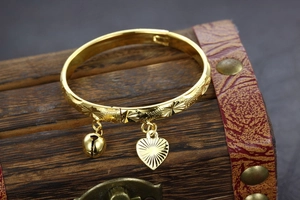 Detail of gold-plated copper child bangle with engraved stars, heart, and bell charms