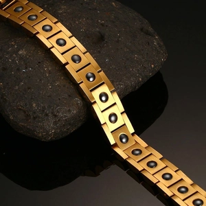 Macro shot of gold-plated stainless steel magnetic bracelet on black raw stone surface
