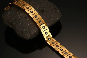 Close-up of gold-plated magnetic link bracelet with round black stone inlays on dark rock