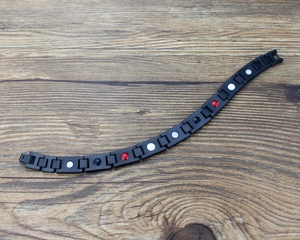 Detalle macro de la pulsera magnética de acero negro con elementos de terapia roja y blanca