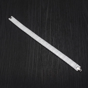Détail d'un bracelet en céramique blanche avec fermoir en métal argenté sur bois sombre