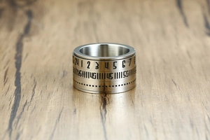Close-up of rotating titanium steel ring featuring engraved Arabic numerals on wooden table