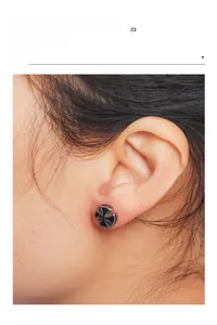 Close-up of retro stainless steel cross stud earring worn on ear showing detail