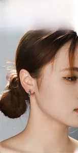 Detailed view of a silver titanium steel cross hoop earring worn on a model's earlobe