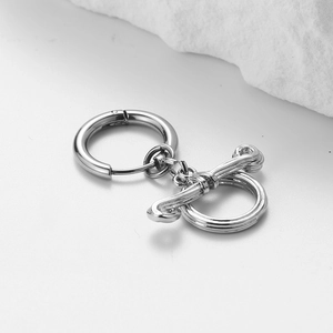 Orecchino a cerchio in acciaio inox con ciondolo a chiusura OT su sfondo di pietra