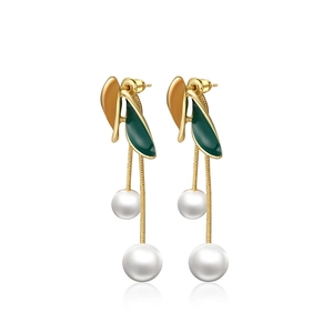Détail de boucles d'oreilles pompon dorées avec feuilles en émail vert foncé et perles blanches