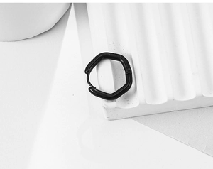 Vue macro d'une boucle d'oreille hexagonale en acier titane noir mat sur un support texturé blanc