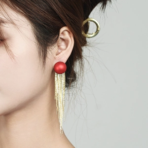 Detailansicht roter mattierter Kugelohrringe mit goldenen Quasten an Model