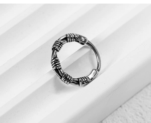Close-up of vintage industrial hoop earring with barbed wire texture in aged silver finish