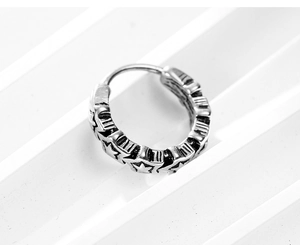 Macro shot of silver retro hoop earring with embossed pentagram patterns in punk style