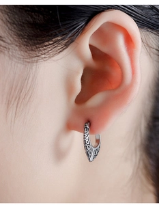 Macro shot of retro silver engraved hoop earrings with ornate vine textures on ear