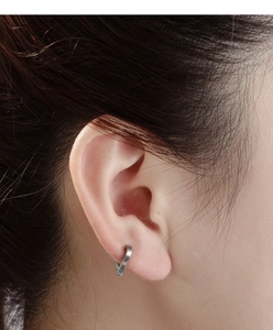 Macro shot of a silver minimalist geometric cross earring on model's ear with metal texture
