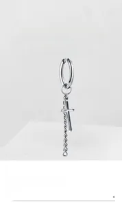 Detail of silver stainless steel cross earring with rope chain on minimalist background