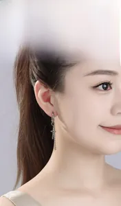 Detailed view of silver cross earring with long metal chain on ear model in gothic style