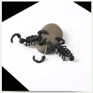 Punk style black scorpion stud earrings displayed on pebble stones with a matte finish