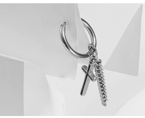 Detailed view of silver cross earring with metal chain on a minimalist paper display