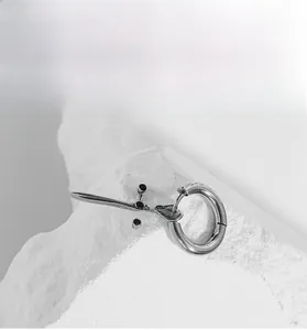 Detail of gothic stainless steel sword earring with hoop on a textured stone surface
