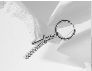 Macro shot of silver titanium steel cross earring with chain on white stone texture