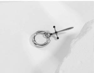 Macro view of stainless steel cross sword earring on natural rock textured surface
