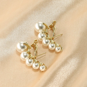 Elegant gold pearl earrings with a curved wheat-ear design on luxury champagne satin fabric