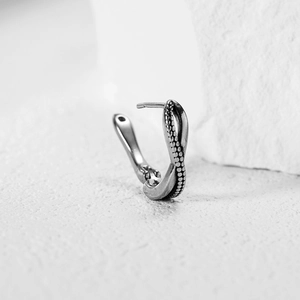 Vintage silver twisted cross hoop earring with grainy texture on white stone background