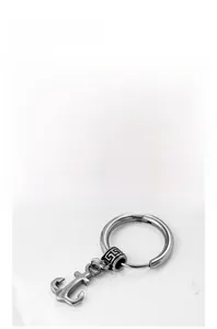 Detail of silver anchor pendant earring with Greek fret pattern bead on white sand