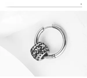 Vue macro d'une boucle d'oreille créole en acier avec un pendentif cylindre étoile