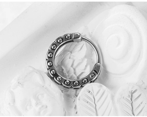 Macro shot of silver hip-hop hoop earring with metallic studs on a white plaster background